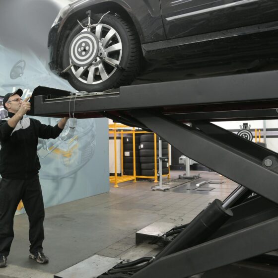 serious mechanic checking car wheels on lift in modern car service garage