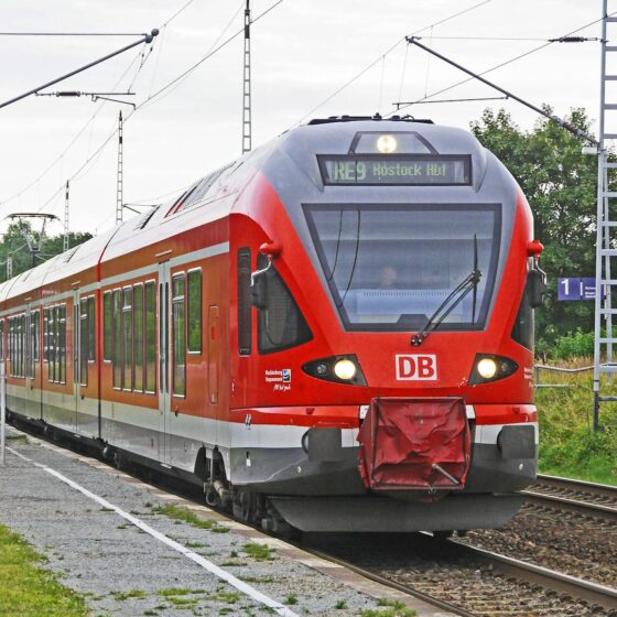 red train on tracks with green grass beside under bright sky