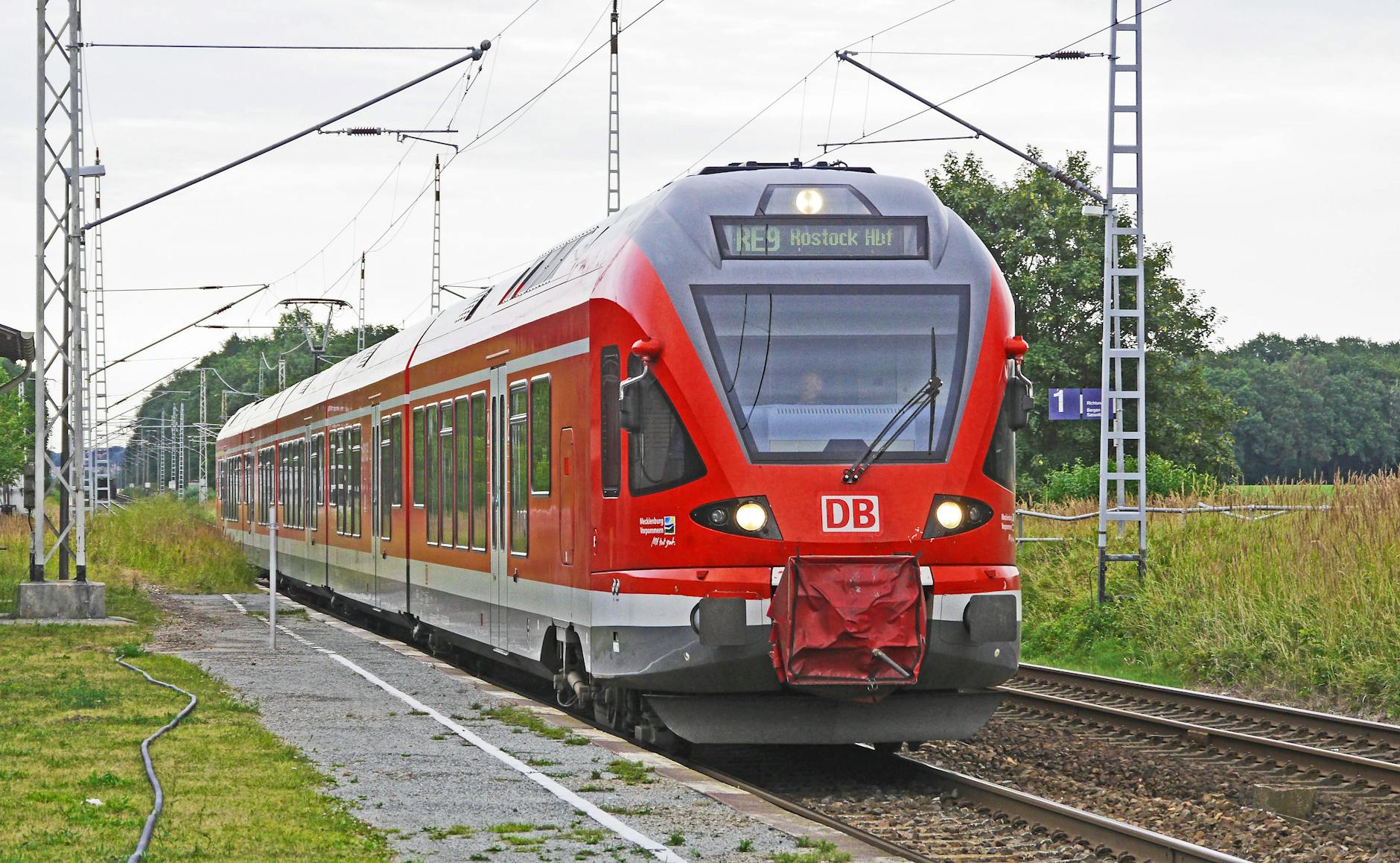 red train on tracks with green grass beside under bright sky