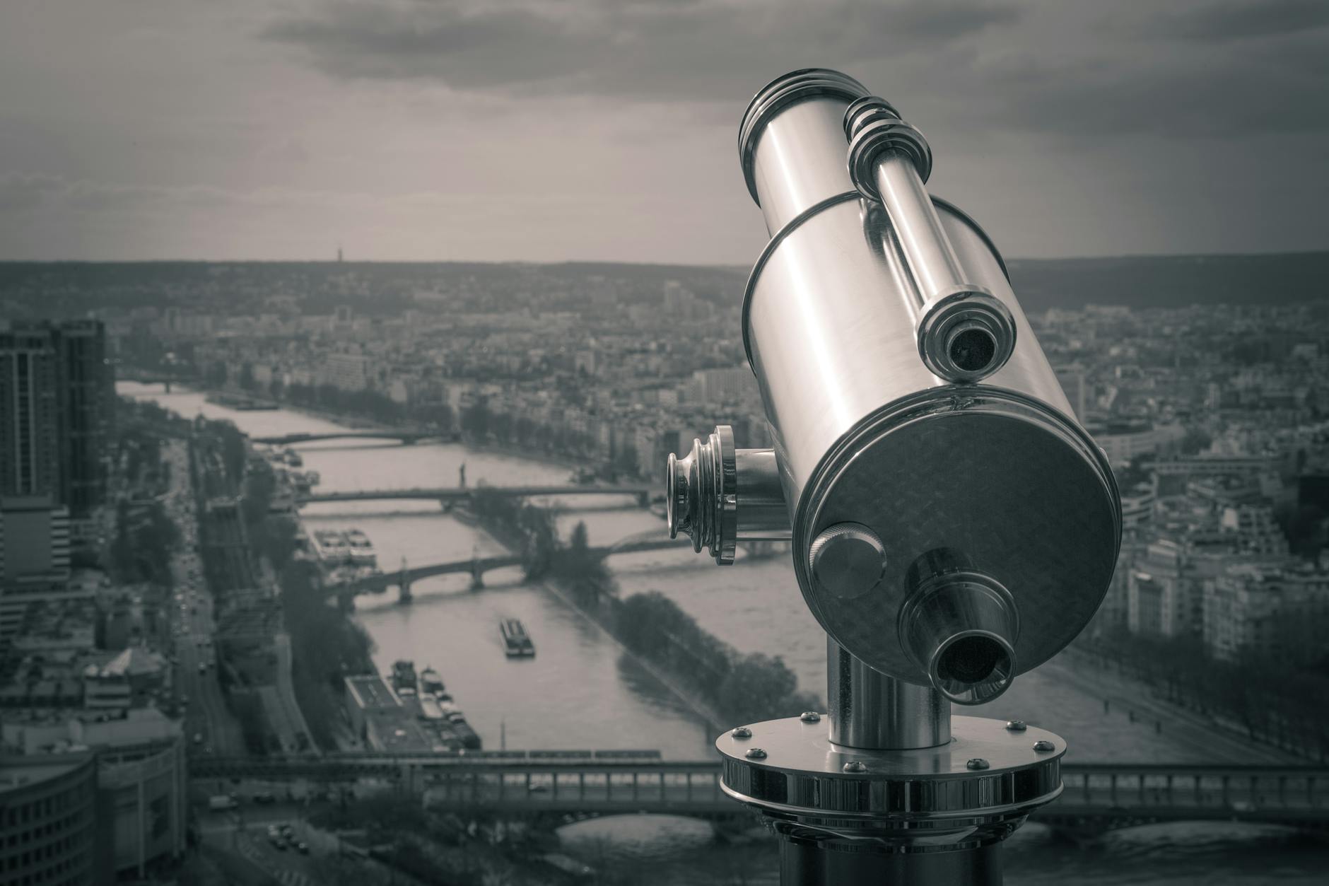 grayscale photography of observation telescope overlooking city riverbank